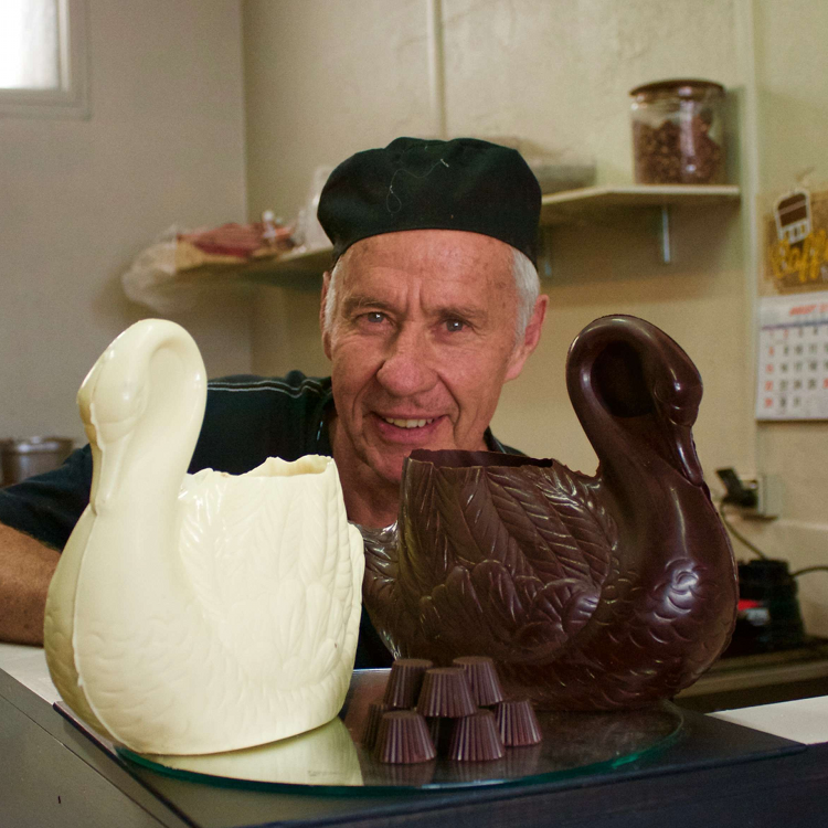 Chocolate Creator Gavin standing behind some chocolate swans, one is white choclate, one is milk chocolate there are also some truffles sitting in front of the swans