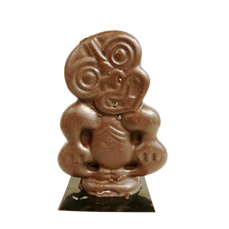 Three dimensional chocolate tiki sitting down, head cocked to one side and hands on it's knees