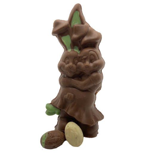Two chocolate bunnies giving each other a hug with a small white chocolate egg in front of them.