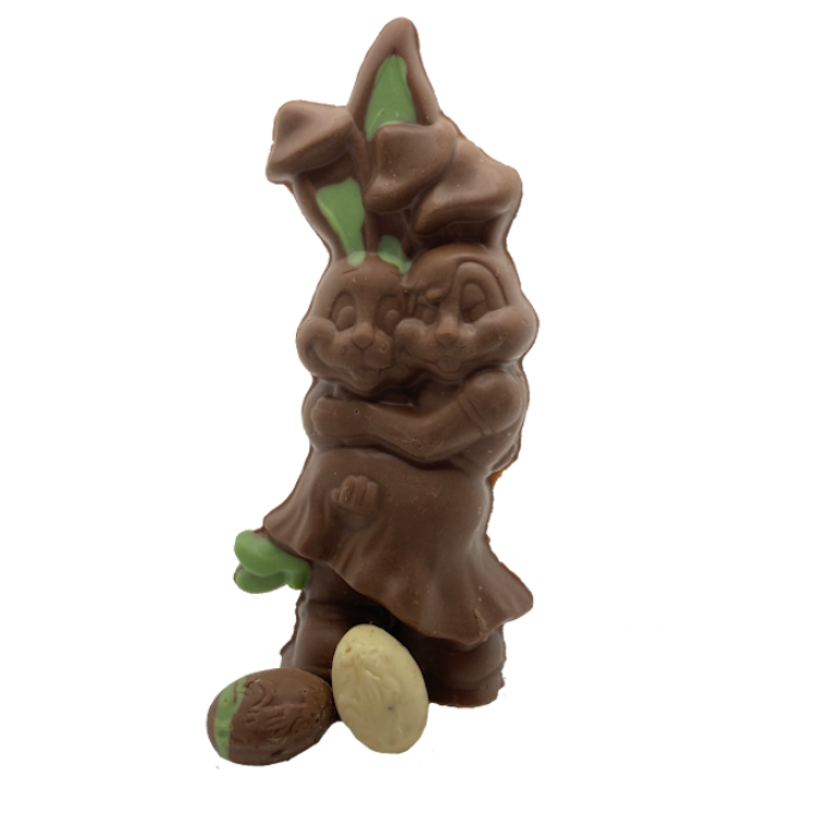 Two chocolate bunnies giving each other a hug with a small white chocolate egg in front of them.