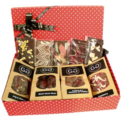 A red spotted box with lid and ribbon containing a mixture of Giles chocolatier bars and truffles